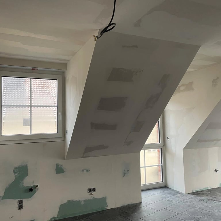 Zabudowa poddasza z płyt gipsowo-kartonowych, widoczne skosy, okna dachowe i przygotowanie ścian do malowania.