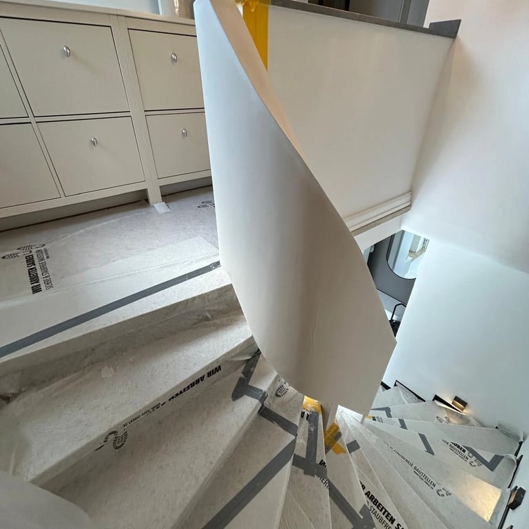 Zabudowa poręczy schodowej w trakcie montażu, płyta gipsowa osłaniająca metalową konstrukcję, zabezpieczone stopnie taśmą och