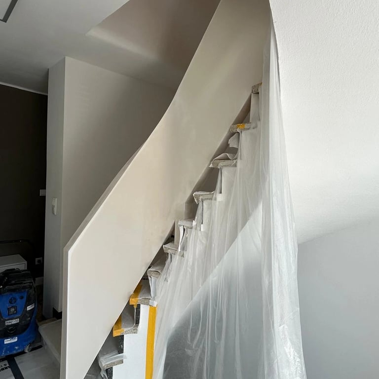 Zabudowa poręczy schodowej na etapie wykończenia, gładka powierzchnia płyty gipsowej, schody zabezpieczone folią i taśmą.