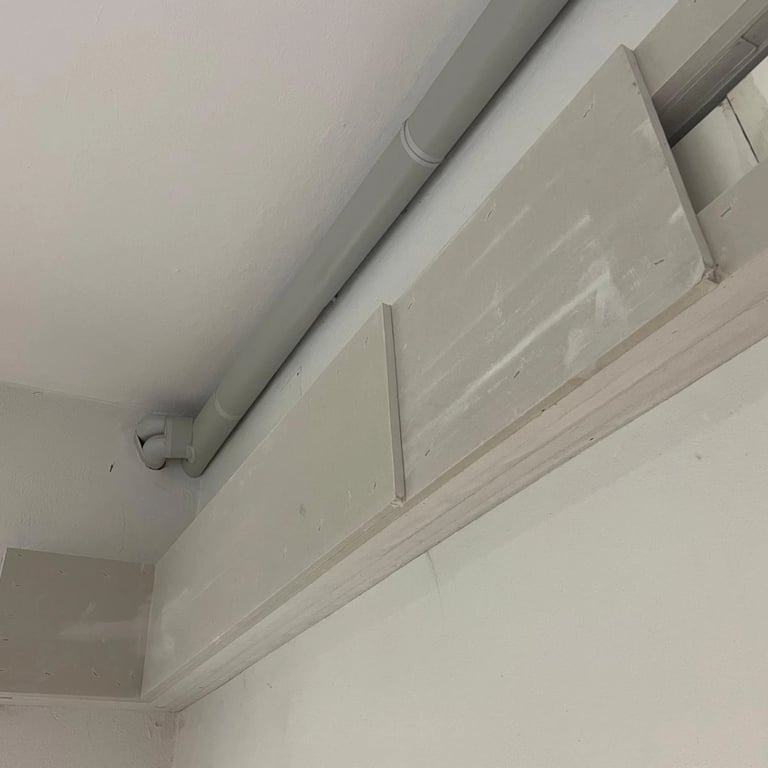 Zabudowa przeciwogniowa wokół rury instalacyjnej przy suficie, płyty ognioodporne zamontowane na konstrukcji.