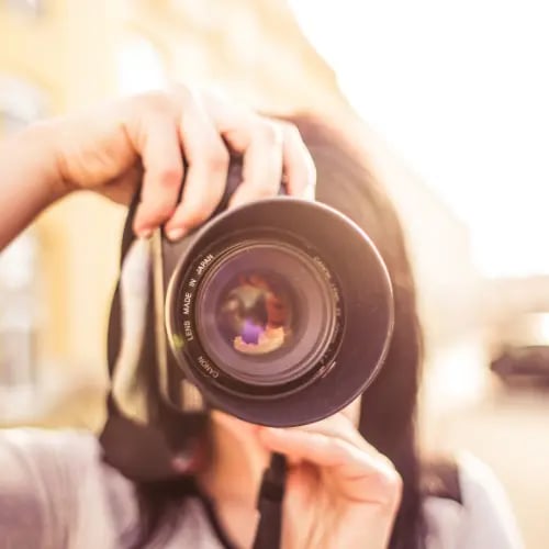 Professional photographer holding a DSLR camera with a wide lens during an outdoor golden hour photoshoot.