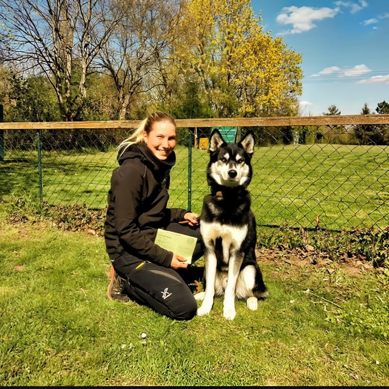 A smiling woman posing with her Alaskan Husky dog at an outdoor obedience training school.