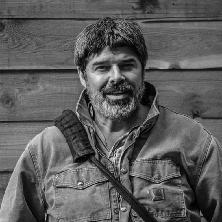 a man with a camera bag in front of a wood plank wall