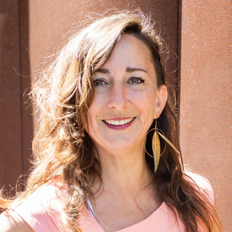 a smiling woman with long hair and golden leaf earrings