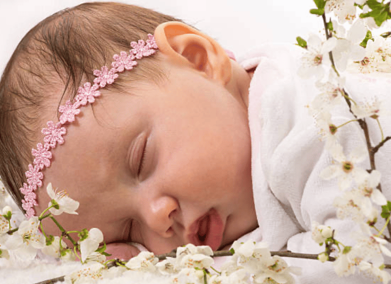 a baby lying on her front, wearing garland of flowers around her head