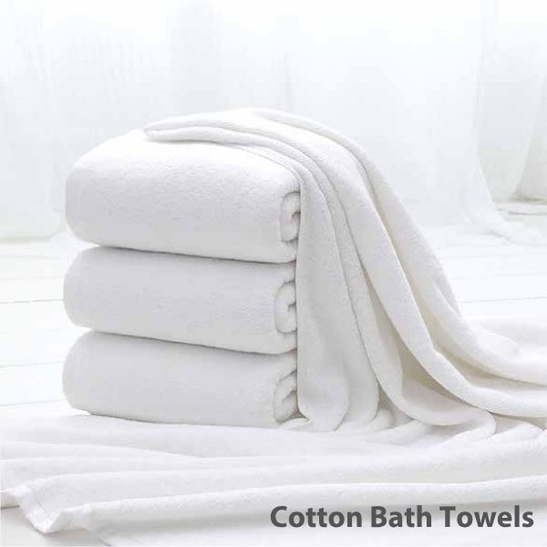 a stack of Cotton Bath towels and towels on a bed