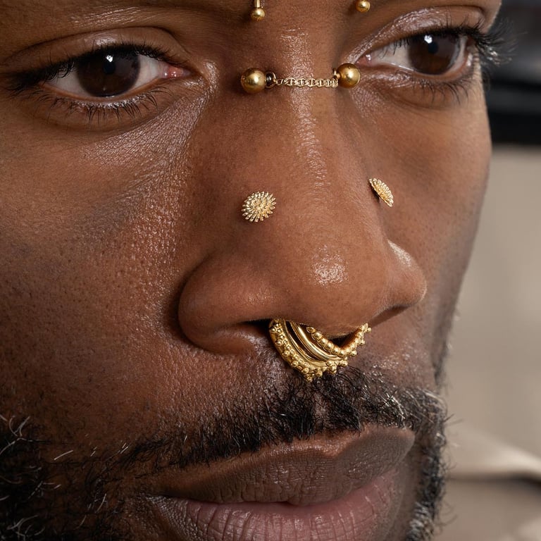 Extreme close-up of a man's face featuring an ornate gold septum ring and a chain bridge piercing