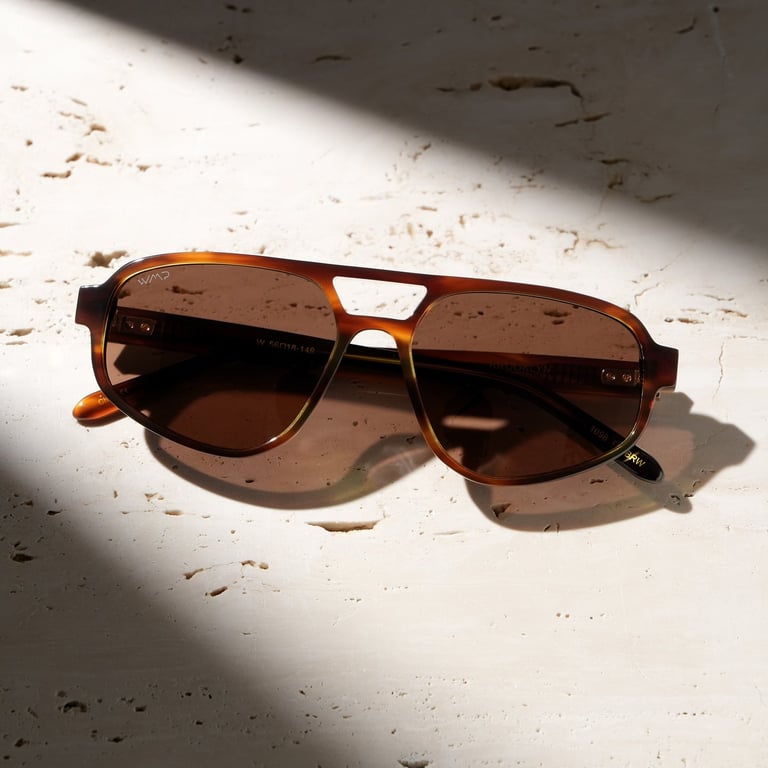 Tortoiseshell aviator sunglasses with brown lenses on textured white surface, lit softly for e-commerce photography