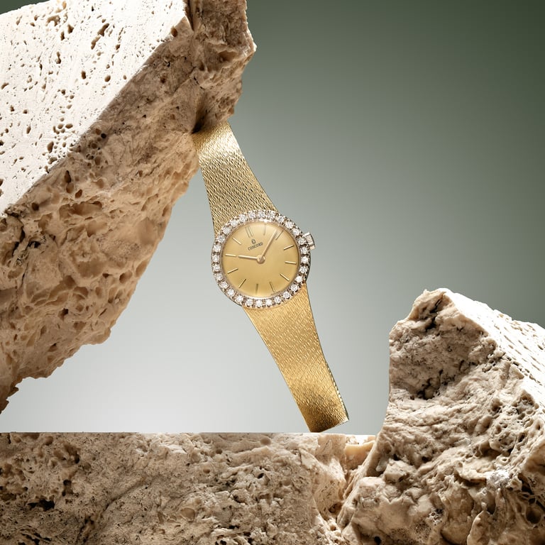 Elegant gold watch with diamond bezel, draped over textured stone against a soft green background for e-commerce photography