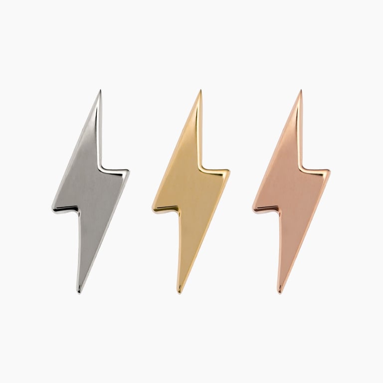 Metallic lightning bolt-shaped stud earrings, one silver, one gold, and one rose gold, on a solid background