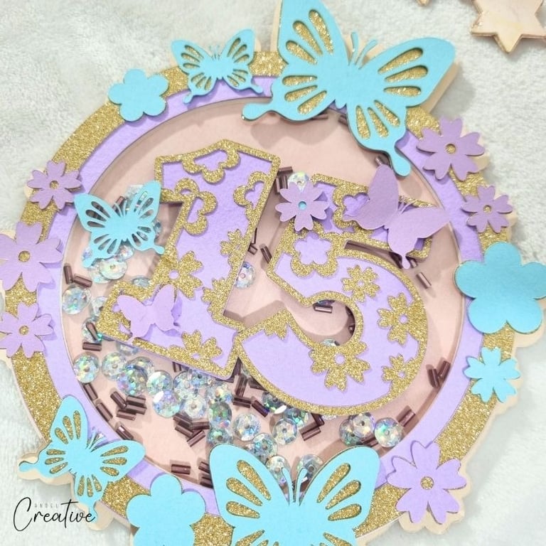Round cake topper, shaker, in pastel purple and blue with gold accents with number 15 inside.