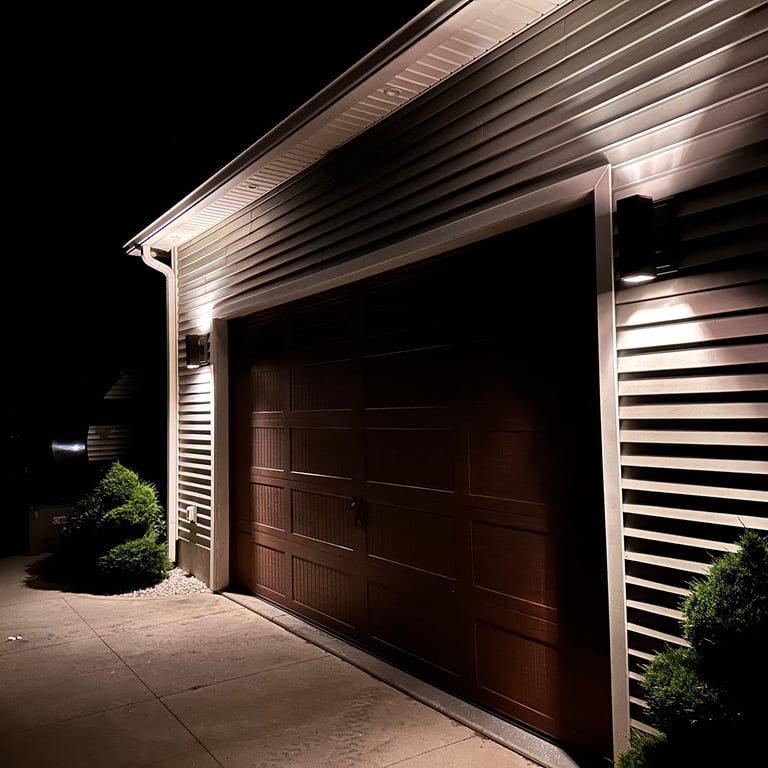 Modern outdoor garage wall sconces illuminating a brown garage door and vinyl siding at night.