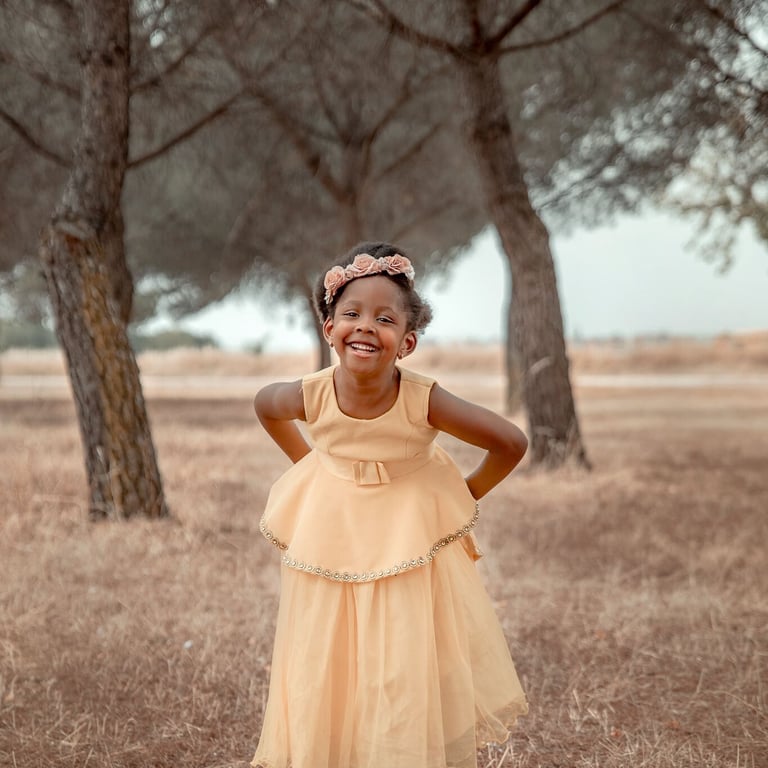 niña con vestido amarillo sonriendo en campo de pinos