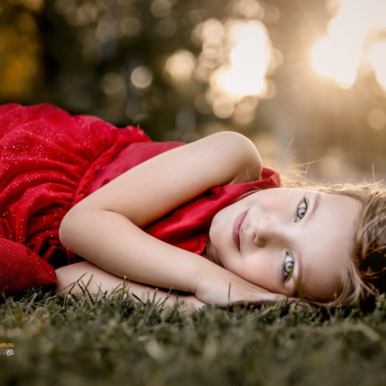 niña de ojos claros tumbada en el cesped con vestido rojo