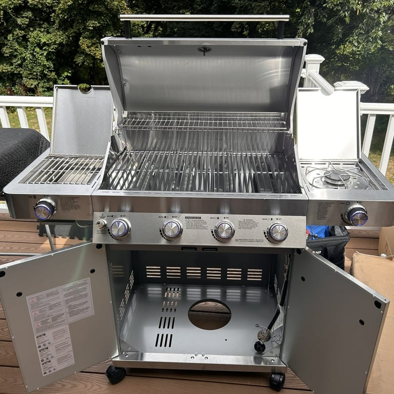 Stainless steel Monument brand 4-burner propane grill with doors, covers and hood open.
