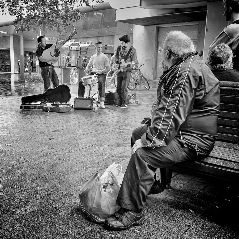 Composition in street photography by Peter Pickering shows man watching musicians perform