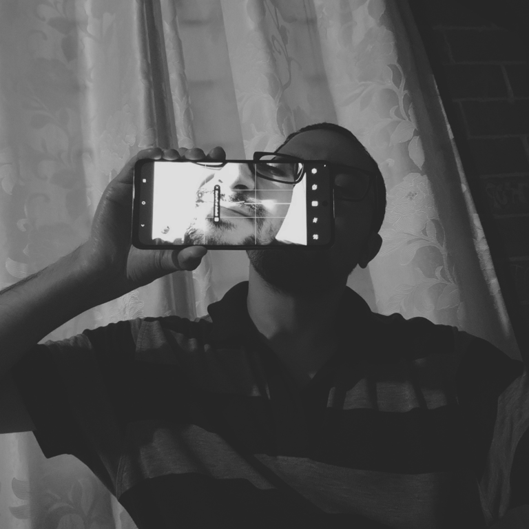 Black-and-white self-portrait with a cell phone obscuring part of the face.