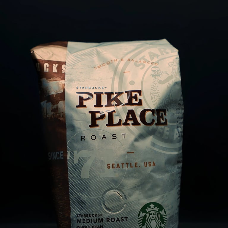 A bag of Pike Place Medium Roast Coffee Beans from Starbucks beside a mug of coffee beans on a reflective table surface.