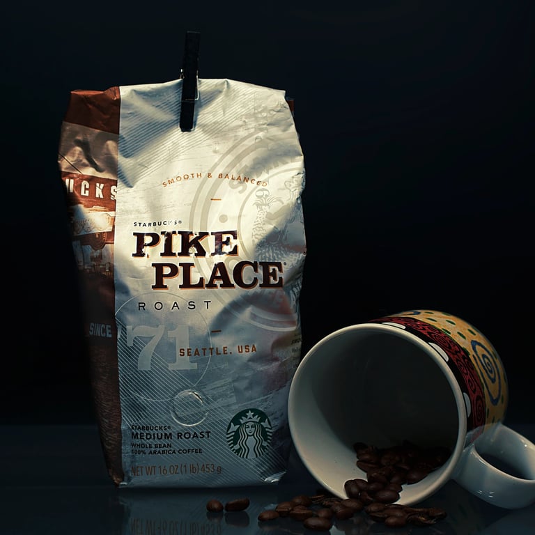 A bag of Pike Place Medium Roast Coffee Beans from Starbucks beside a mug of coffee beans on a reflective table surface.
