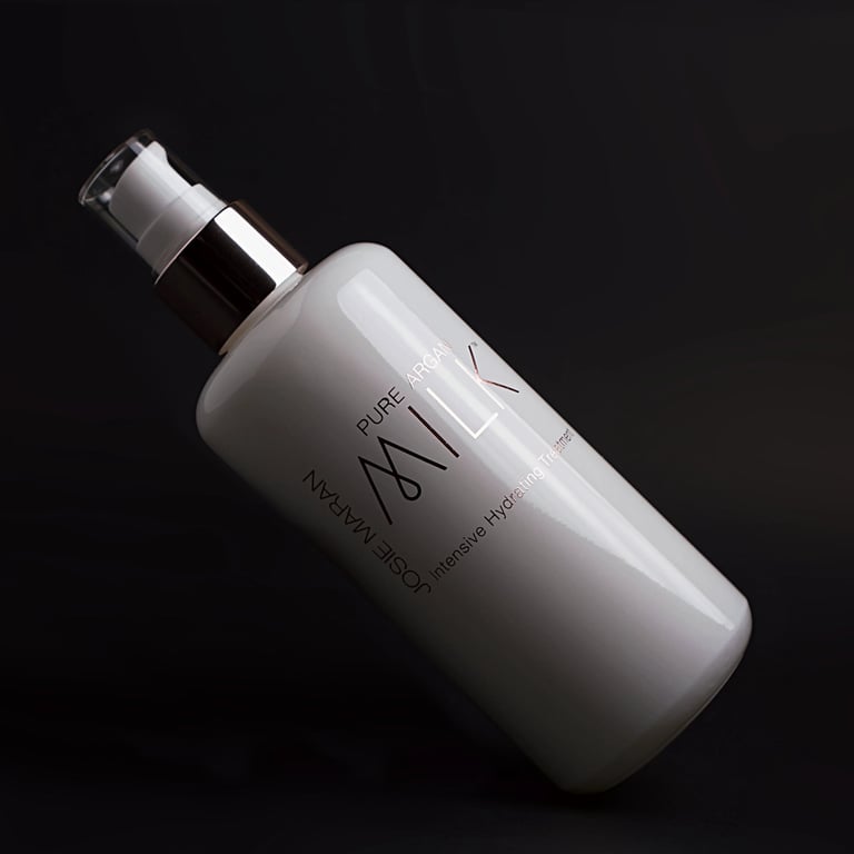 Bottle of Josie Maran Pure Argan Milk product photo shoot on black backdrop.