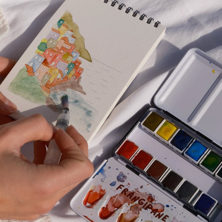 Un artiste réalise une aquarelle représentant des maisons de village côtier dans un carnet de croqui