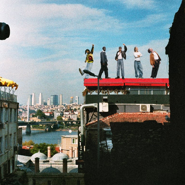 A group of diverse friends in casual fashion posing on an urban rooftop overlooking a scenic city skyline.