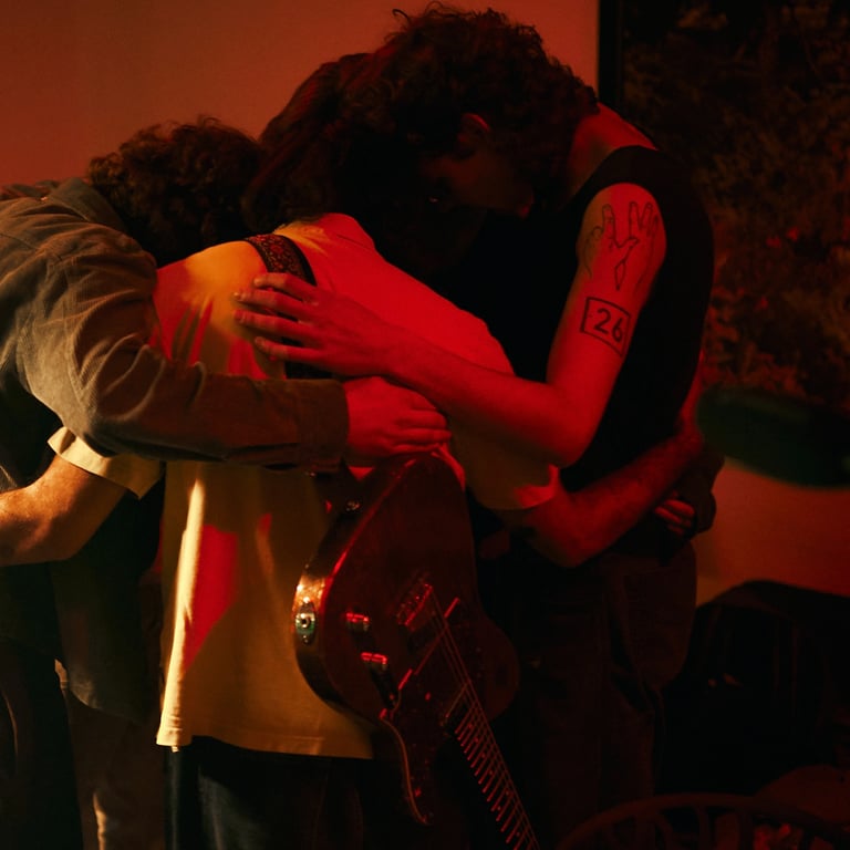 Band members in a huddle with an electric guitar under moody red stage lighting.