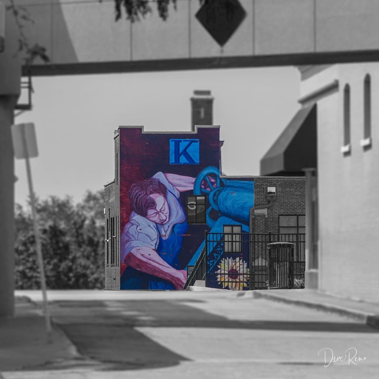 Urban mural of a labor figure on the Kansan Building, with selective color against a grayscale streetscape.