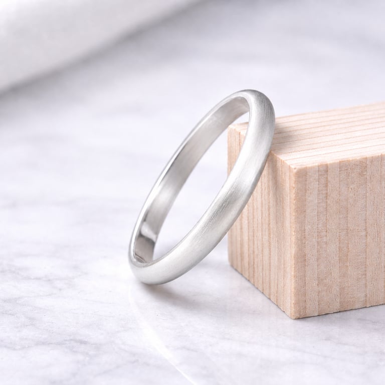 Brushed 999 fine silver wedding band resting on a wooden block over a white marble surface.