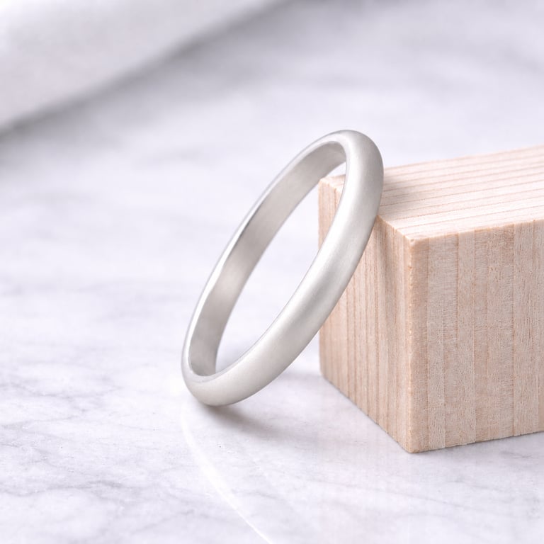 Satin matte 999 fine silver wedding band leaning against a small wooden block on a marble surface.