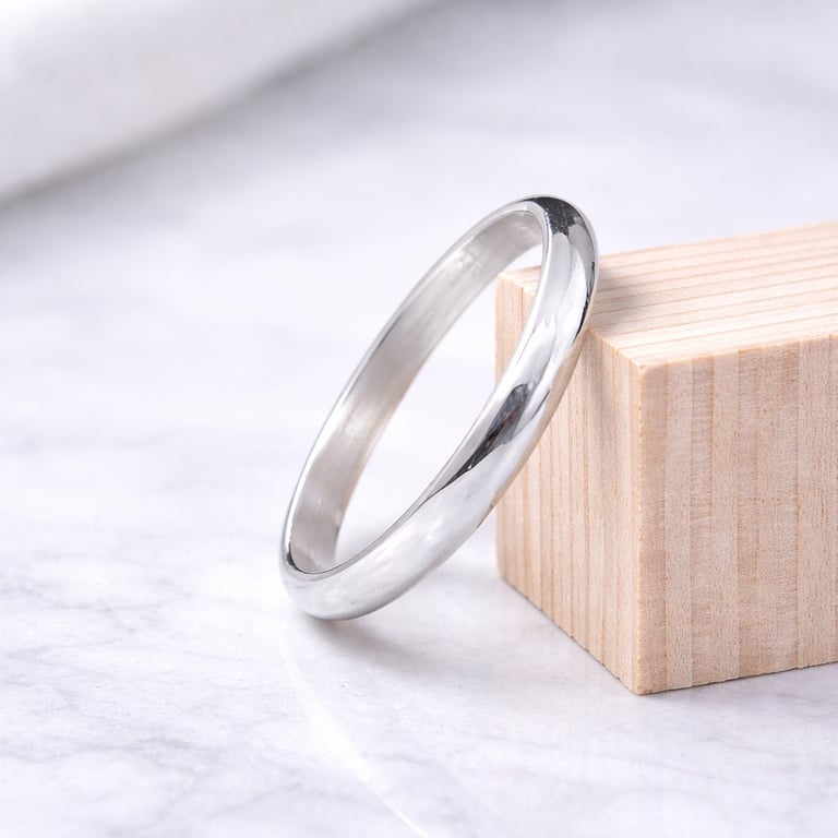 Minimalist polished 999 fine silver wedding band resting on a wooden block over a marble surface.