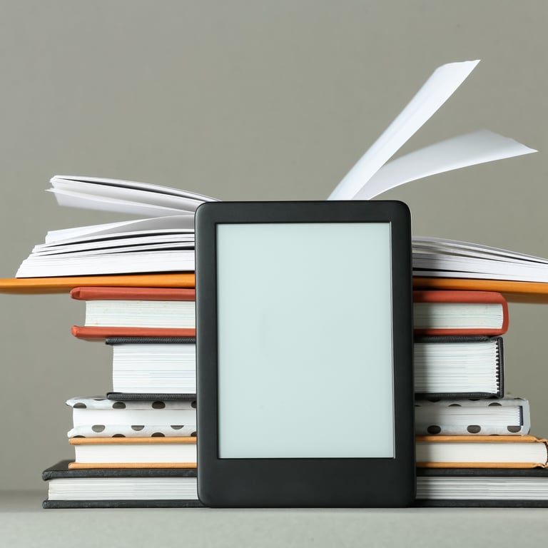 An e-reader with a blank screen leans against a stack of hardcover books with fluttering pages.