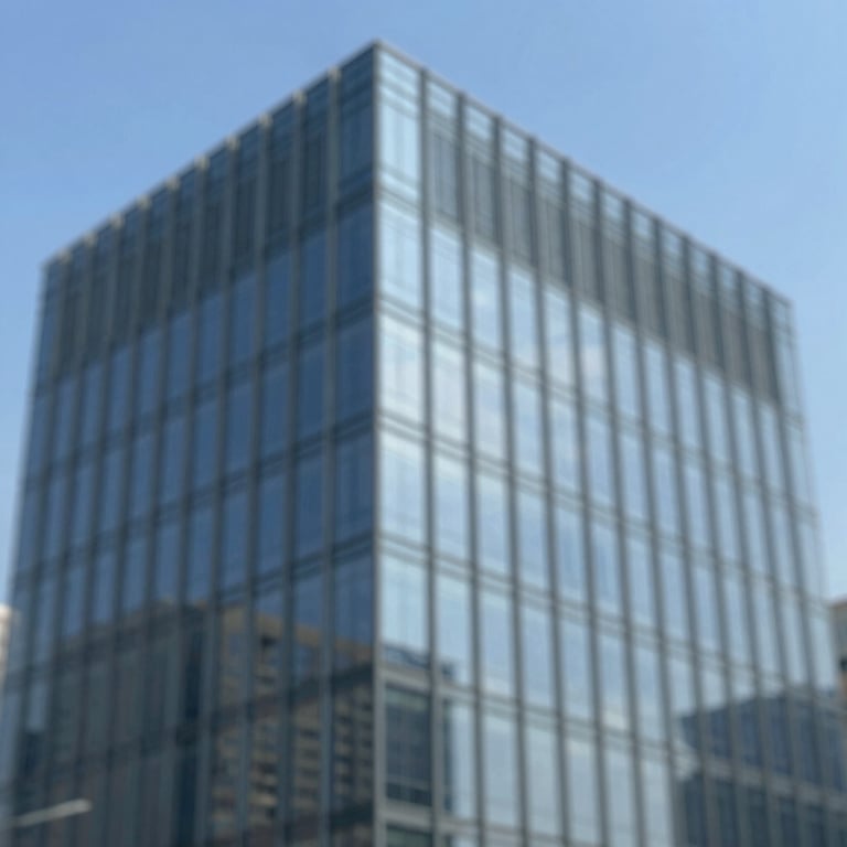 An architectural shot of a modern glass building reflecting the blue sky.