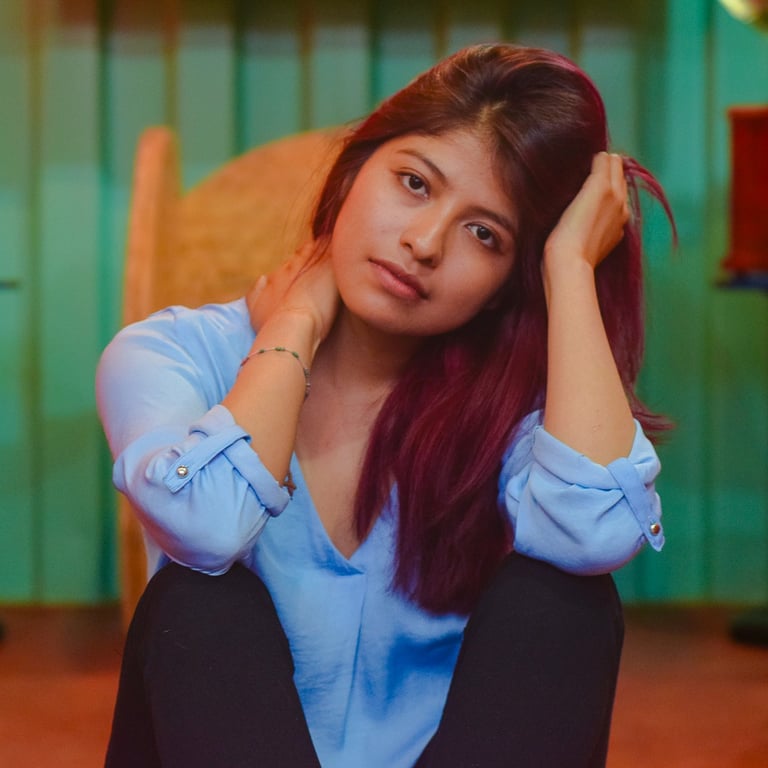 Young woman with long red hair posing in a blue shirt against a teal background.
