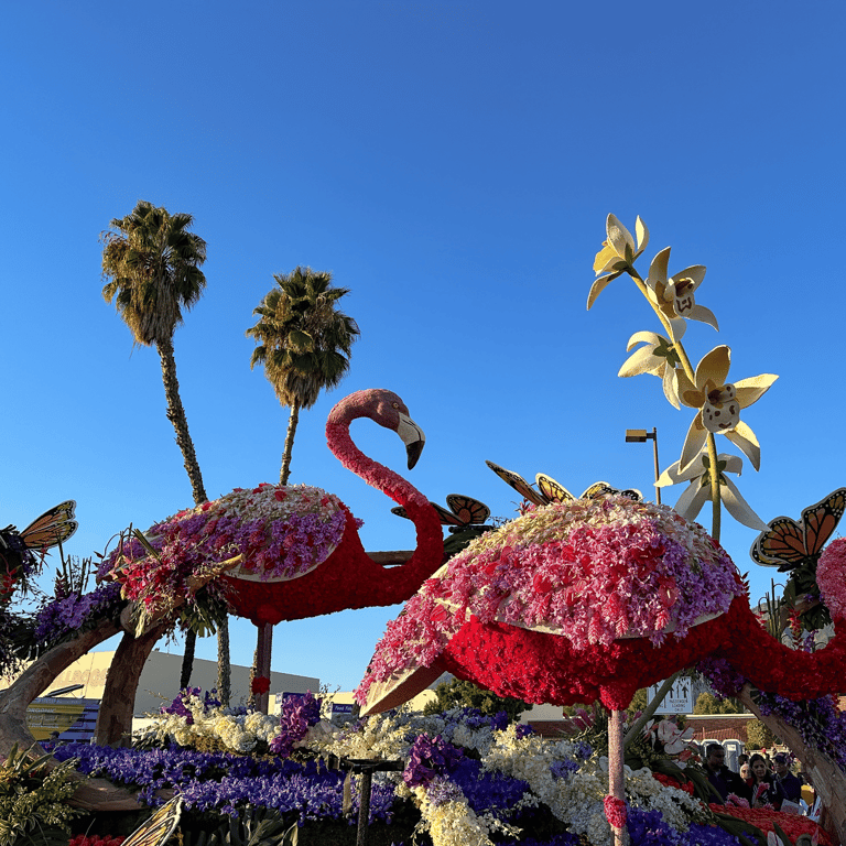 Floral parade float featuring pink flamingos and monarch butterflies under a clear blue sky.