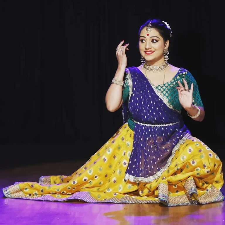 A Kathak dancer performing in traditional yellow and blue attire with ornate Indian jewellery.