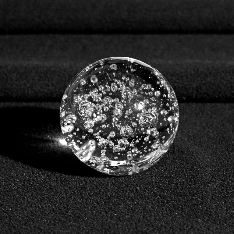 A clear glass sphere with bubbles inside, resting on a textured black surface.