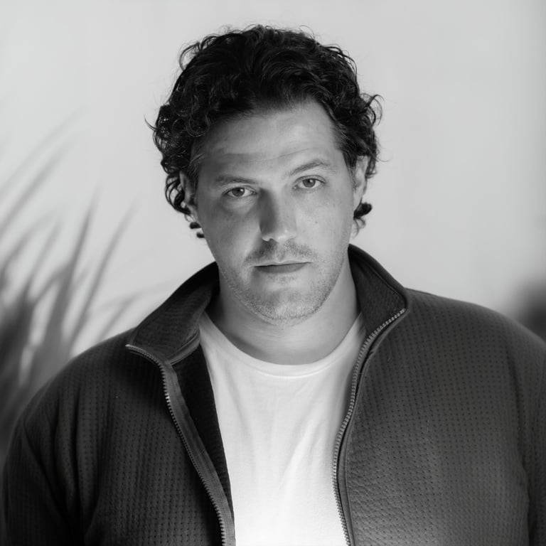 Black and white portrait Drai Cabello with curly hair wearing a zip-up jacket over a white t-shirt. 