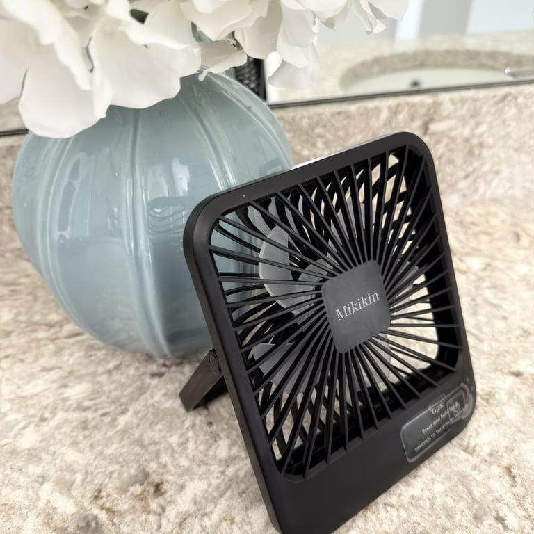 Small folding travel fan sitting on a bathroom counter for cooling during hotel stays