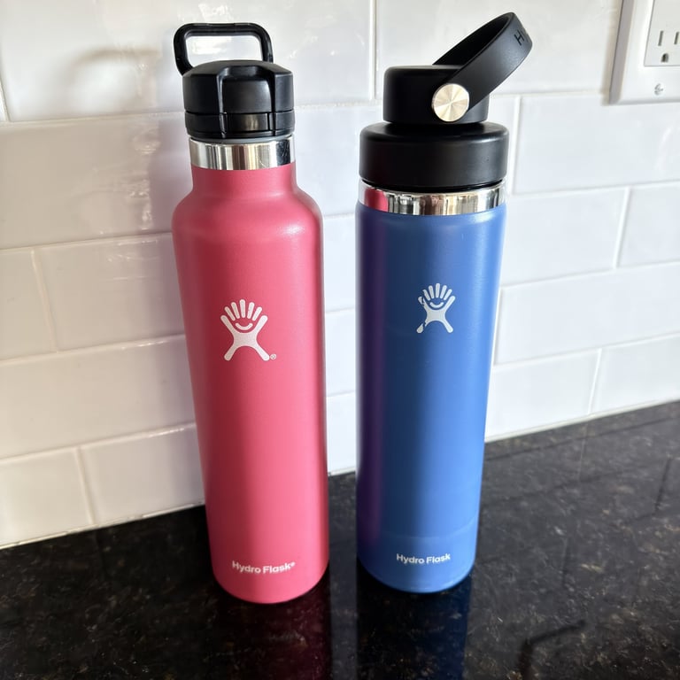 Pink and blue Hydro Flask bottles on a kitchen counter used for daily travel hydration