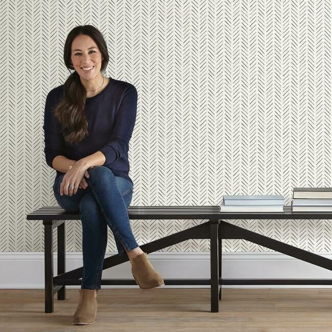Joanna Gaines sits on a black bench against black and white herringbone peel and stick wallpaper.