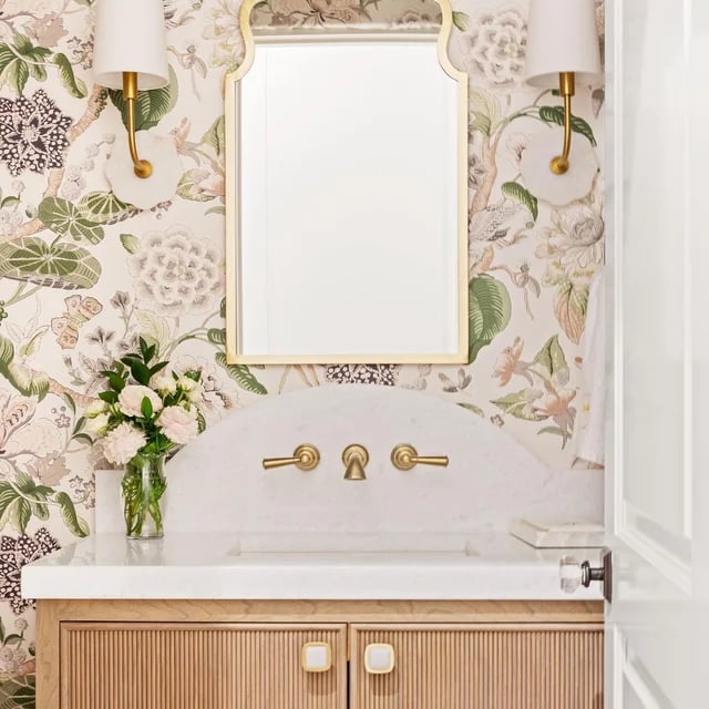 Elegant bathroom vanity with floral wallpaper, gold mirror, and marble countertop.