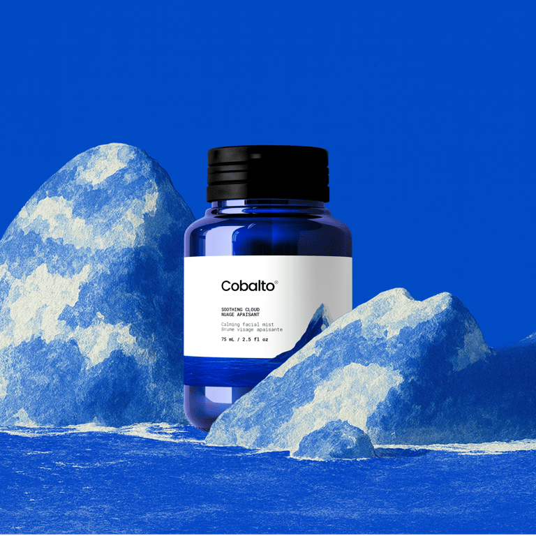 Frasco azul da marca Cobalto em destaque sobre fundo surrealista com montanhas em tons de azul claro