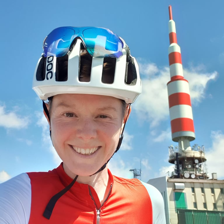 Picture of LIz Hughes dressed in cycling kit, at the top of a mountain, smiling.