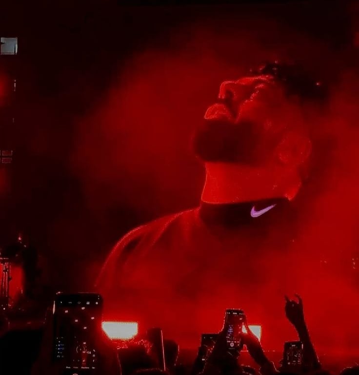 badshah performing on stage under red lights during a live concert with fans recording on phones.