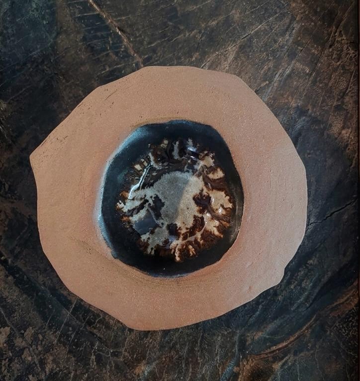 Handmade ceramic clay bowl with a dark glazed center resting on a rustic wood surface.