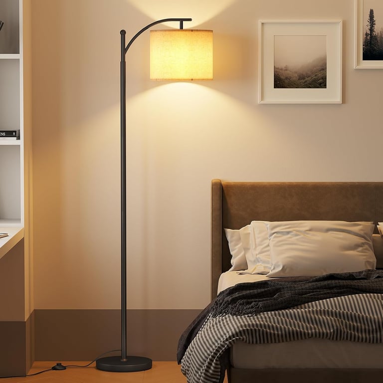 Modern black arc floor lamp with a linen drum shade illuminating a cozy bedroom bedside.