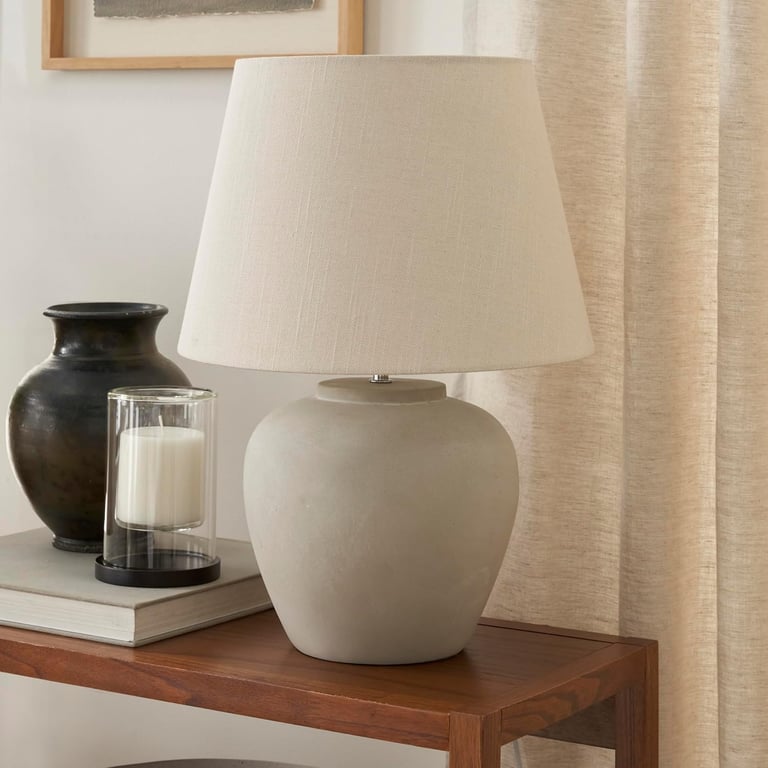 Modern concrete table lamp with a beige linen shade on a wooden side table with decor.