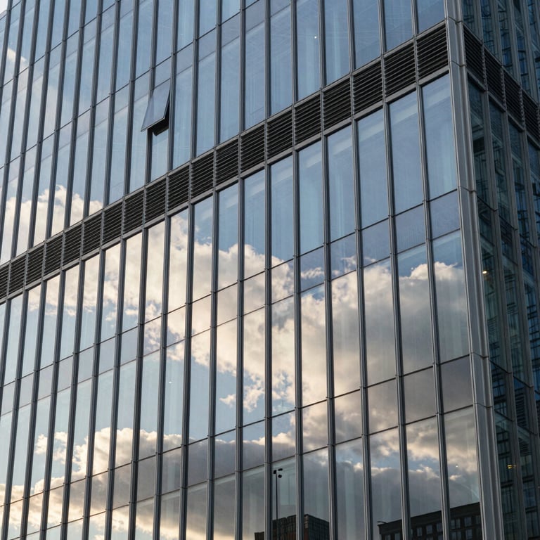 A modern office building with a glass facade reflecting the morning sky and white clouds, emphasizing stability and innovation.