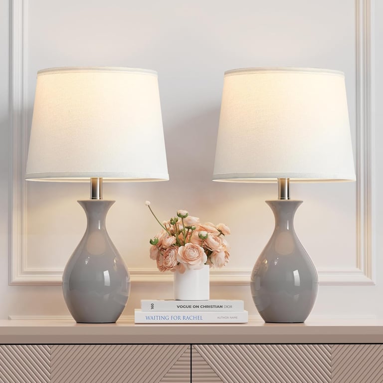 Pair of gray ceramic table lamps with white drum shades on a console table.